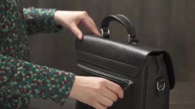 Kadın eli, erkek siyah deri çantasının fermuarını kapatıyor. İzole edilmiş, kahverengi arka planda.