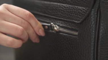 Siyah erkek deri çantasının fermuarını açan ve kapatan güzel manikürlü bir kadın eli videosu. İzole edilmiş, bulanık arkaplanda