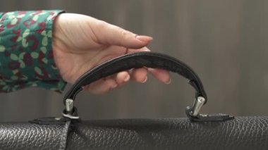 Kadın elinin çıplak manikürlü, çantanın sapını tutan ve siyah deri çantayı alan yakın plan bir gösteri videosu. Zarif erkek çantası.