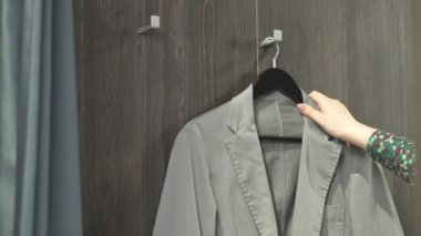 Soyunma odasına erkek ceketi getiren yakın plan bir tezgahtar. Bir müşteriye kıyafet teklif etmek. Değişik seçenekler. Marka kıyafetler.
