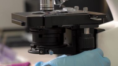 Biyolojik örnekleri test etmek için mikroskop kullanan bir tıp laboratuarı çalışanı. Sıvıyı ve profesyonel ekipmanları inceliyor. Yakın plan, bulanık arkaplan