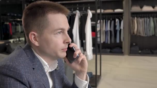 Bonito Homem Está Sentado Sofá Confortável Falando Telefone Boutique Roupas — Vídeo de Stock