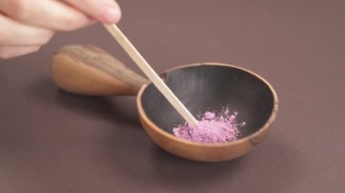 El işi kozmetikler. Tahta kaseye organik bitkisel tozu karıştıran bir kadının yakın çekimi. Doğal kozmetik hazırlığı