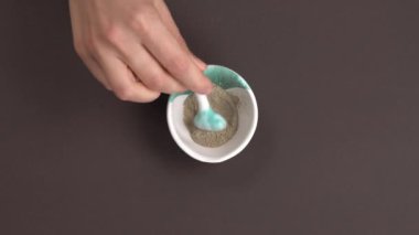 Organik bitkileri kaşıkla seramik kaseye karıştıran bir kadının üst görüntüsü. El yapımı kozmetik ürünleri yapmak