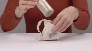 Kurumuş organik kök tozuyla birlikte cam şişeyi pamuk torbaya koyan bir kadının yakın çekimi. El işi kozmetikler, doğal ürünler. İzole edilmiş, bulanık arkaplanda