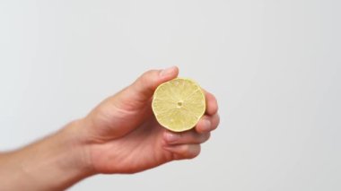 Erkek elin bir dilim limonu tutarken ve sıkarken yakın plan. Citrus suyu hamurdan ve damlalardan akar. İzole edilmiş, beyaz arkaplanda