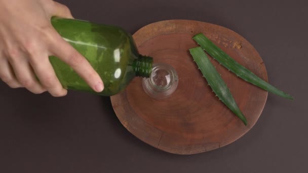 アロエベラジェル 天然有機更新化粧品 スキンケアの概念 緑のペットボトルから透明なガラス容器にゲルを注ぐ女性の手のトップビュー — ストック動画