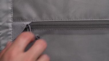 Gri seyahat çantasındaki bir cebin fermuarını açan erkeğin yakın çekim gösterisi. Şık bir aksesuar. Seyahat ve bagaj konsepti.
