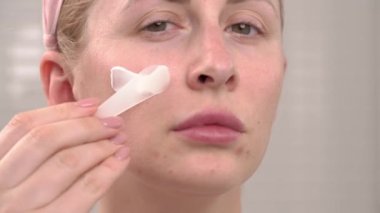 Güzel kadının yüzünün mükemmel cildiyle yakın çekimi nemlendirici krem sürerek kozmetik kepçe kullanıyor. Güzellik kavramı, kremler, cilt bakımı ve berraklığı.