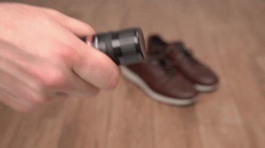 Ön planda kahverengi ayakkabı boyama kremini açan erkek eli yakın plan. Bulanık arka planda erkek kahverengi deri ayakkabılar.