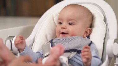 Bebek koltuğunda oturan ve annesiyle oynayan sevimli küçük çocuk. Mutlu çocuk portresi. Gerçek duygular. Anne çocuğuyla oynuyor..