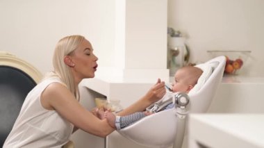 Şefkatli, neşeli, genç bir annenin küçük oğluna gülümsemesi ve kaşıkla beslemesi. Anne sevimli çocuğunu emziriyor.