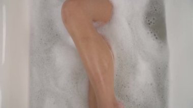 Güzel vücutlu, köpükle banyo yapan ve erotik bir şekilde kendine dokunan seksi bir genç kadının alt kısmı..