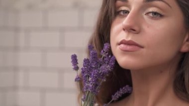 Genç romantik bir kadının portresi. Elinde lavanta rengi bir buket tutarken ve vücuduna çiçeklerle dokunurken. Seksi ve erotik atmosfer