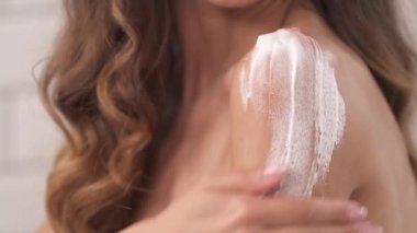 Genç ve güzel bir kadın omzunun derisine nemlendirici köpük sürüyor. Günlük cilt bakımı ve hijyen. Yakın çekim gösteri videosu