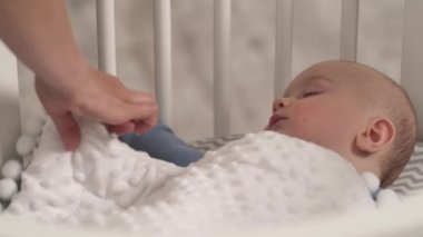 Sevgi dolu anne ellerinin oyuncağı uyuyan çocuğun yanına koyması. Sevimli erkek bebek yatağında uyuyor..