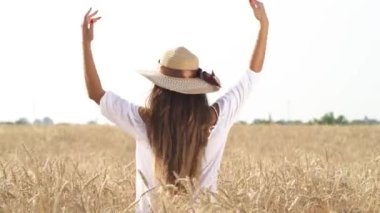 Hasır şapkalı genç kadın gün batımında altın buğday tarlasının ortasında ellerini kaldırıyor. Romantik atmosfer kavramı