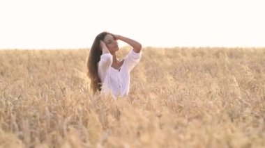 Güzel kumral dalgalı saçları olan, saçlarına dokunan ve gülümseyen çekici romantik bir kadın. Altın buğday tarlasında bir kız.