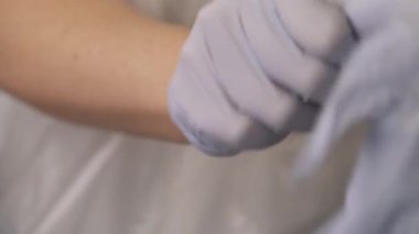 Profesyonel bir kozmetik uzmanının kozmetik prosedürüne başlamadan önce beyaz lateks koruyucu eldivenler giymesi. İzole edilmiş, bulanık arkaplanda