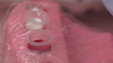 Masaya kırmızı mürekkep yakın plan. Kozmetik uzmanı, dudaklarında kalıcı makyaj için dövme makinesi hazırlıyor. Dermapigmentasyon prosedürü uzmanı.