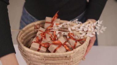 Kahverengi kağıda sarılı küçük dikdörtgen hediye kutularını alan ve hasır sepetten kırmızı kurdelelerle süslenmiş bir kadın..