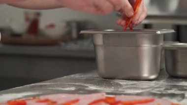 Restoran mutfağı. Profesyonel pizzacının yakın plan çekimi pizzaya dilimlenmiş kırmızı biber koyuyor. Seçici odak atışı