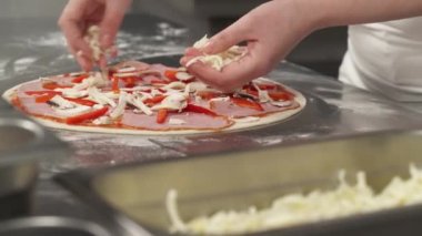 Şef fırıncının profesyonel mutfakta pizza yaptığı yakın çekim. Peynir pizzanın üstüne düşer. Peynir tabakasını pizza üzerine hizalıyorum.
