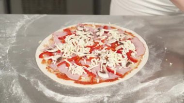 Şef fırıncının profesyonel mutfakta pizza yaptığı yakın çekim. Profesyonel aşçı pizzaya peynir katıyor.