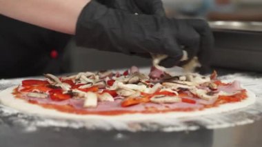Profesyonel mutfakta pizza yapan siyah lateks eldivenli aşçı. Peynir pizzanın üstüne düşüyor. Peynir tabakasını pizza üzerine hizalıyorum.