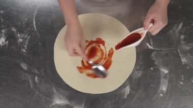 Şef restoranda kaşık kullanarak pizza hamuruna domates sosu sürüyor. İtalyan geleneksel yemek hazırlama.