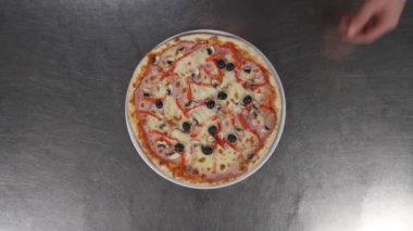 Havadan çekilen görüntülerde erkek elleri lezzetli bir pizzayı metal bir masaya çeviriyor. Geleneksel İtalyan yemeği konsepti