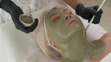 Kozmetik uzmanının hastaların yüzüne ve boynuna kilden maske takması. Cilt bakımı prosedürleri. Cerrahi olmayan kozmetik tedavi