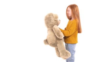 Güzel, kızıl saçlı, gülümseyen ve büyük bir ayı oyuncağı tutan küçük bir kızın yakın plan portresi. İzole edilmiş, beyaz arka planda. Mutlu çocukluk kavramı. Gerçek çocuk duyguları