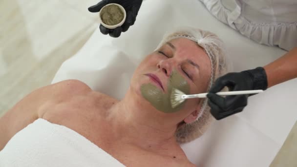 美容师在病人的脸和脖子上涂绿色面膜的头像 专业的护肤程序 抗衰老疗法 — 图库视频影像