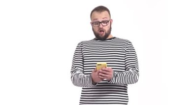 Genç, neşeli bir adam akıllı telefonuna bakarken kameraya suratını ekşitiyor. Yüzünde komik bir ifade olan sakallı adam. Suprasegment. İzole edilmiş, beyaz arkaplanda