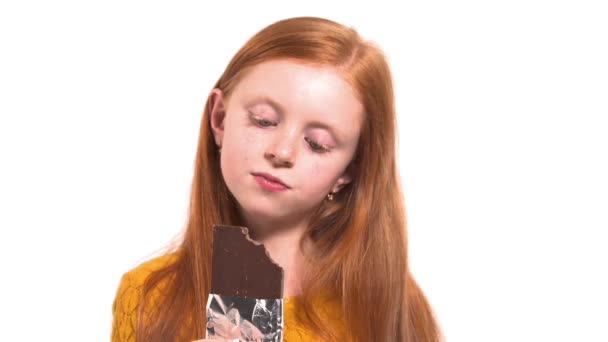 一个红头发女孩的特写 绿色的眼睛咬着一大块巧克力 快乐童年的概念 — 图库视频影像
