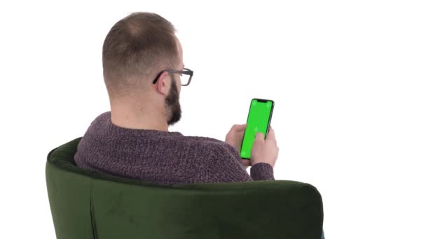 携帯電話を使用して若い男のバックビュー 現代のガジェット使用の概念 男は緑の椅子に座っている 隔離された白い背景に — ストック動画