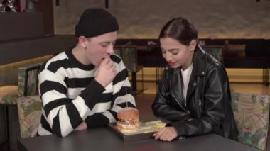 Modern şık bir restoranda hamburger ve patates kızartması yiyen çift. Genç adam sevgili kız arkadaşını patates kızartmasıyla besliyor. Birlikte mutlu anlar
