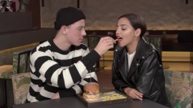 Çift boş modern şık iç lokantada vakit geçiriyor. Genç adam sevimli neşeli kız arkadaşını patates kızartmasıyla besliyor. Gerçek duygular