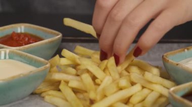 Patates kızartmasını tabaktan alıp beyaz sosa batıran bir kadının sağdan soldan görüntüsü. Şehir yemekleri. İzole edilmiş, bulanık arkaplanda