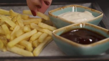 Bir kadının tabaktan bir dilim patates kızartması alıp beyaz sosa batırdığı en alttaki fotoğraf. Sağlıksız gıda konsepti. İzole edilmiş, bulanık arkaplanda