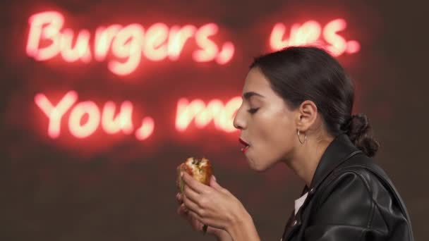 在快餐店里 一个有着浓密黑发的年轻貌美女子正在愉快地吃着新鲜做的大汉堡 美国街头风格的食物概念 复制空间 — 图库视频影像