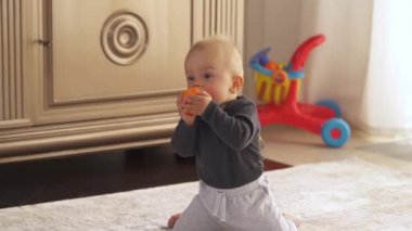 Küçük turuncu top tutan ve çiğneyen sevimli çocuk. Neşeli çocuk oyuncakla oynuyor. Mutlu çocukluk kavramı