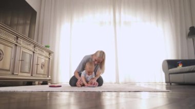 Neşeli genç anne ve küçük oğlu evde birlikte kitap okuyorlar. Aile, çocukluk ve eğlence kavramı