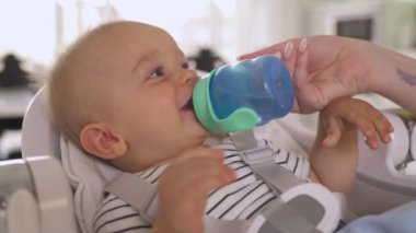 Bebek koltuğunda yatarken gülümseyen küçük bir çocuğun portresi. Şefkatli bir anne oğluna su verir. Bir çocuğa bakıyorum.