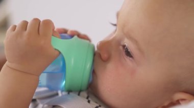 Mavi, dökülmemiş bardağından su içen küçük bir çocuğun yan görüntüsü. İzole edilmiş, bulanık arkaplanda