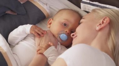 Sevimli küçük tatlı çocuk yatakta yatarken çekici annesi yanında uzanıp onu nazikçe öpüyor. Gündüz uyuyor. Yakın plan..