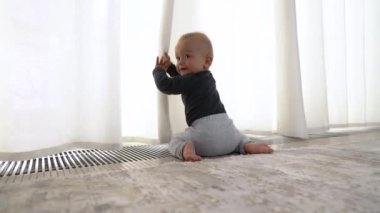 Perdelerle oynayan ve oyuncağına doğru sürünen komik bir çocuğun yakın çekim videosu..