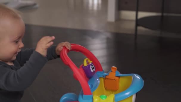 一个快乐的蹒跚学步的男孩带着一辆五颜六色的玩具推车爬行在时尚的室内客厅里的画像 快乐的童年孤立无援 背景模糊 — 图库视频影像