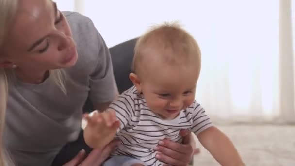 有爱心的母亲和婴儿在家里的地板上玩耍 婴儿翻滚爬行 母亲扶起她的儿子 孩子笑了 真正的情感概念 — 图库视频影像